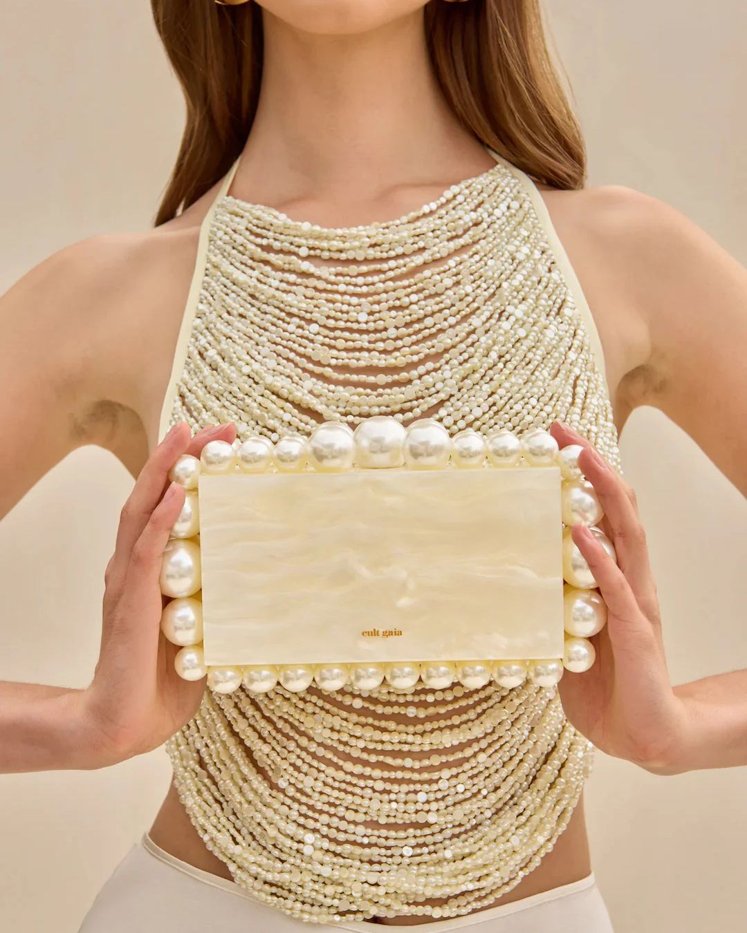 Cult Gaia Lifestyle with Pearl Clutch | Michael Hayes Newport | Michael Hayes Newport Person wearing a multi-strand pearl necklace dress, holding a cream rectangular clutch framed by large pearls.