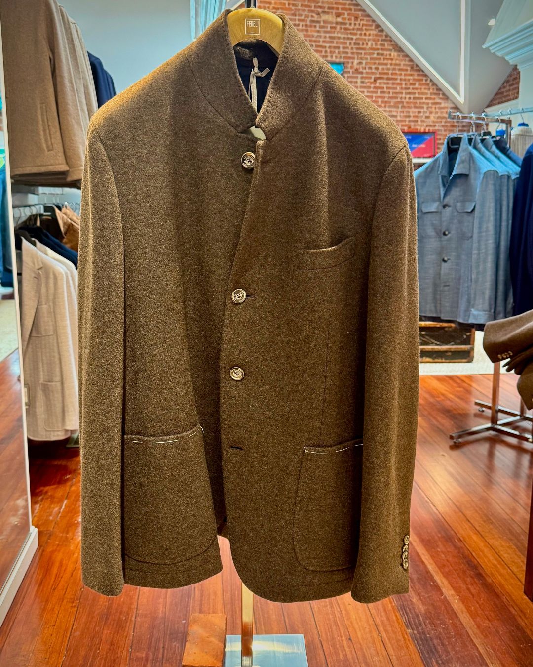 Brown wool overcoat on a hanger in a clothing store, with a notch collar and three front buttons and patch pockets.